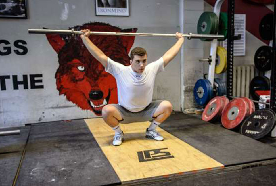 A photo of a man in a bottom squat position as he performs a muscle snatch to overhead squat.
