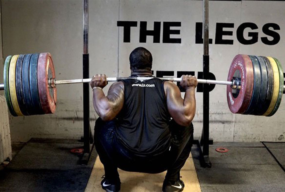 A photo of an athlete performing back squat using heavy load.
